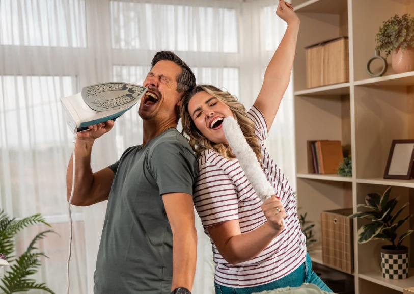 Pareja cantando y bailando en casa, usando un cepillo como micrófono, en un ambiente alegre y relajado.