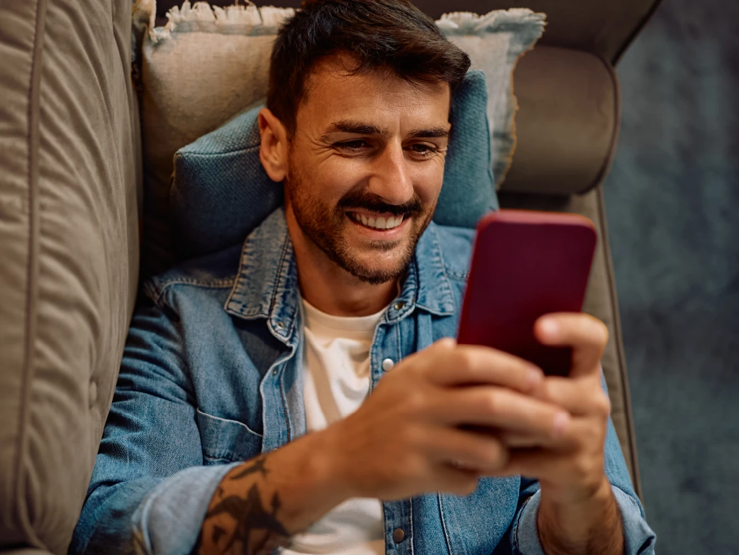 Hombre sonriente descansando en sofá y sosteniendo su teléfono