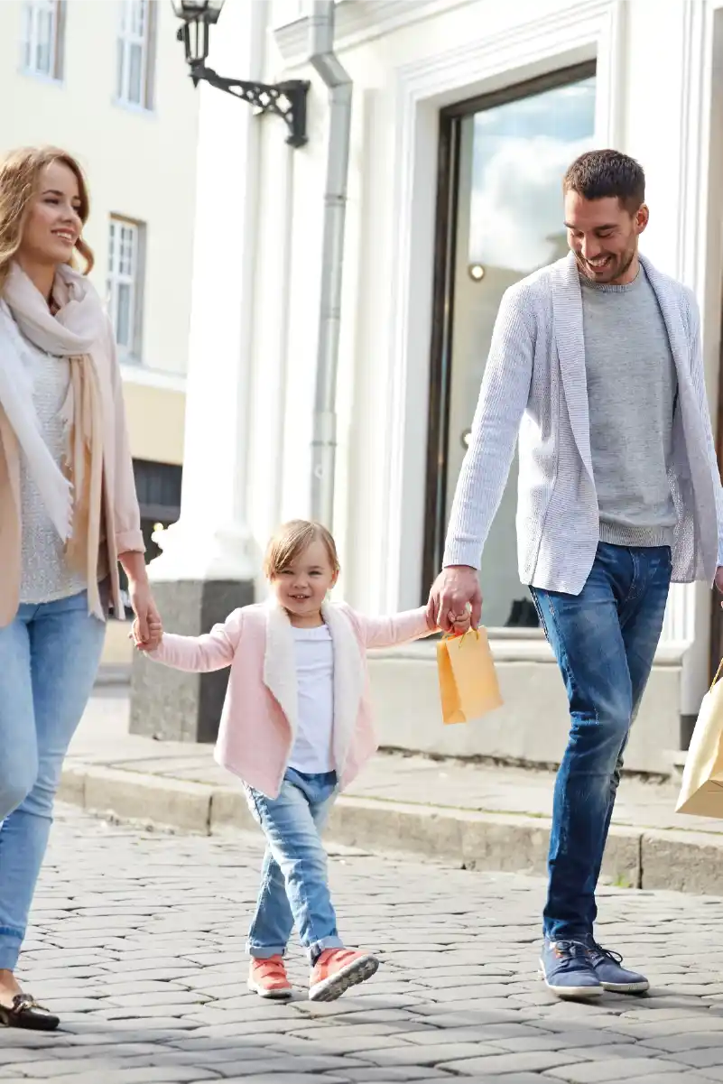 Pareja joven y una niña de la mano llevando bolsas de regalos