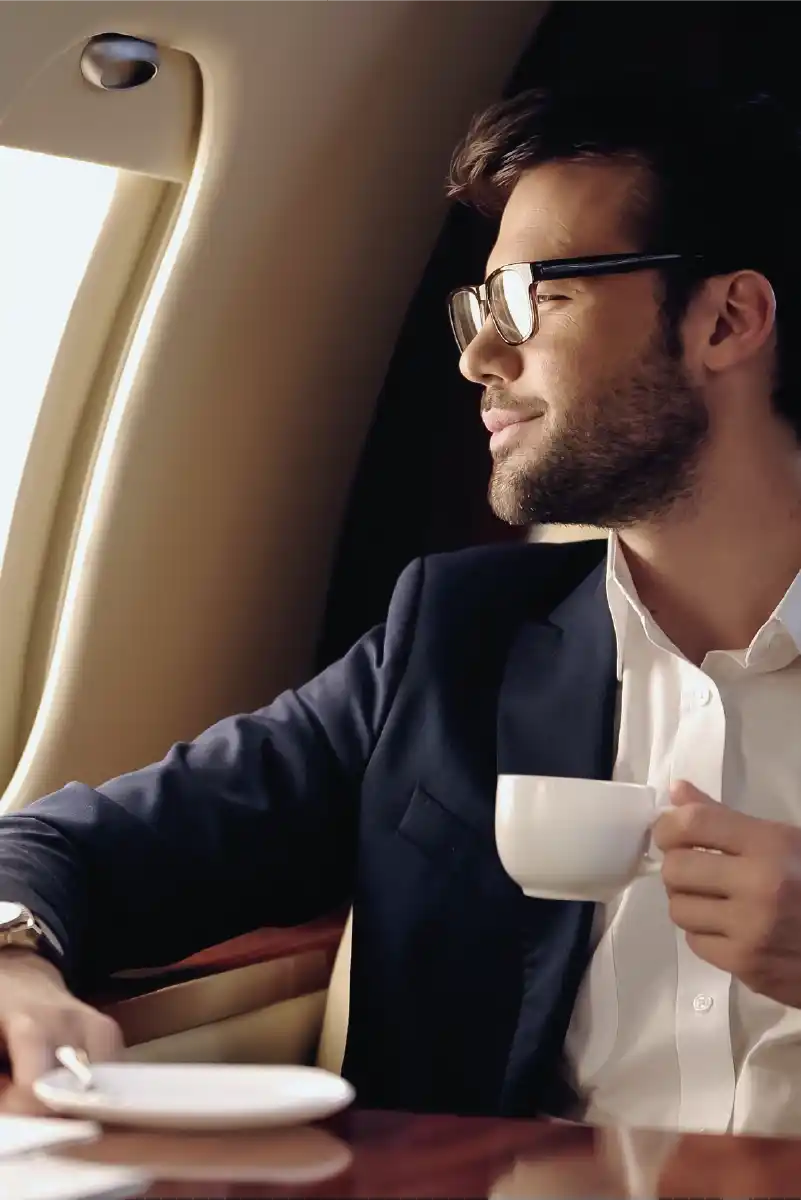 Hombre joven mirando por la ventanilla de un avión, tomando una tasa de café