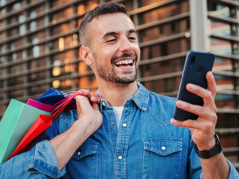 Hombre feliz con bolsas de compras usando su celular