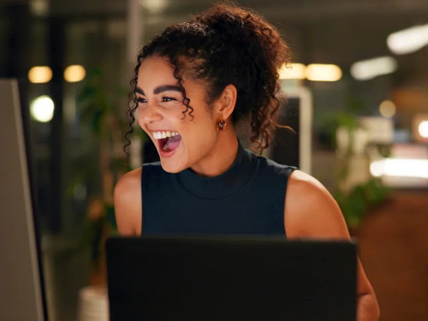 Mujer sonriendo frente a una computadora en un entorno de oficina con iluminación cálida, representando el uso de los beneficios asociados a nómina BCR.
